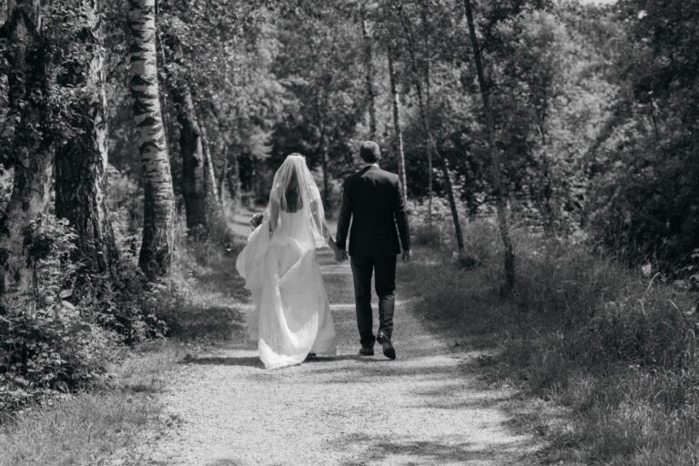 Brautpaar geht Hand in Hand einen Waldweg entlang, Schwarz-Weiß-Aufnahme von hinten