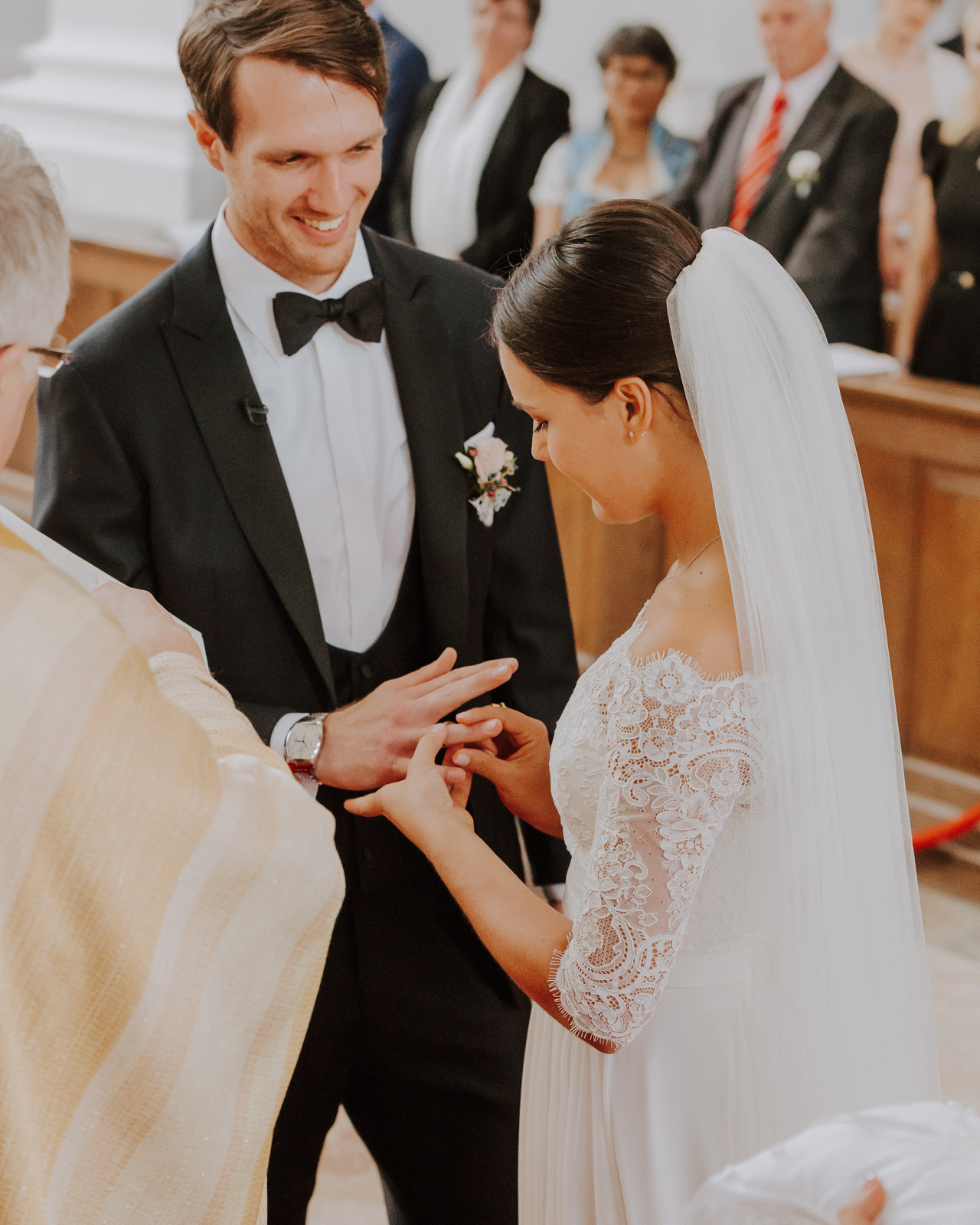 Der Bräutigam bekommt von der Braut den Ehering angesteckt, Trauung in der Kirche mit Gästen im Hintergrund – ein Moment, den ich bewusst ungestellt fotografieren wollte.