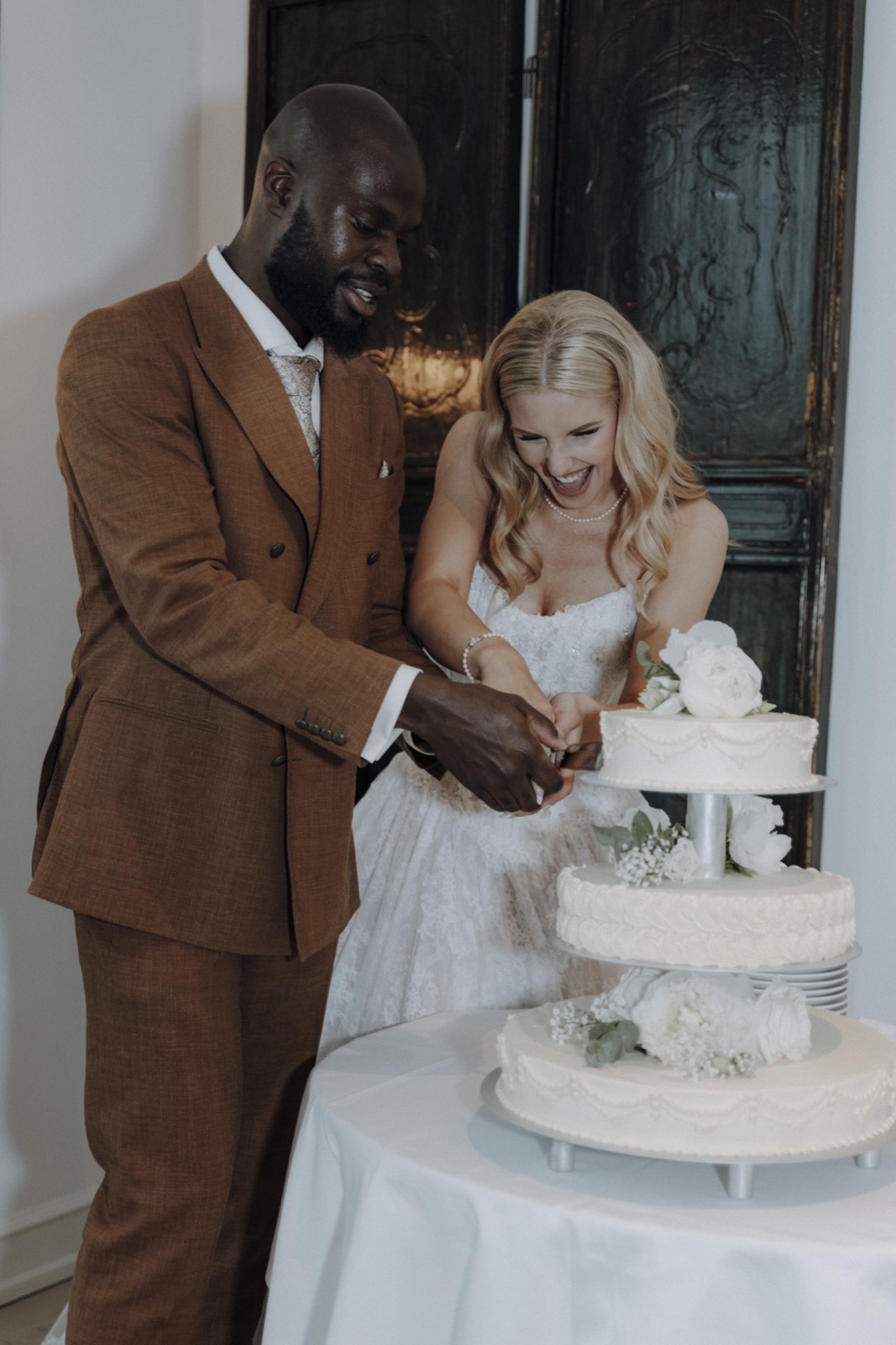 Hertta und Ovie schneiden lachend gemeinsam ihre dreistöckige Hochzeitstorte an