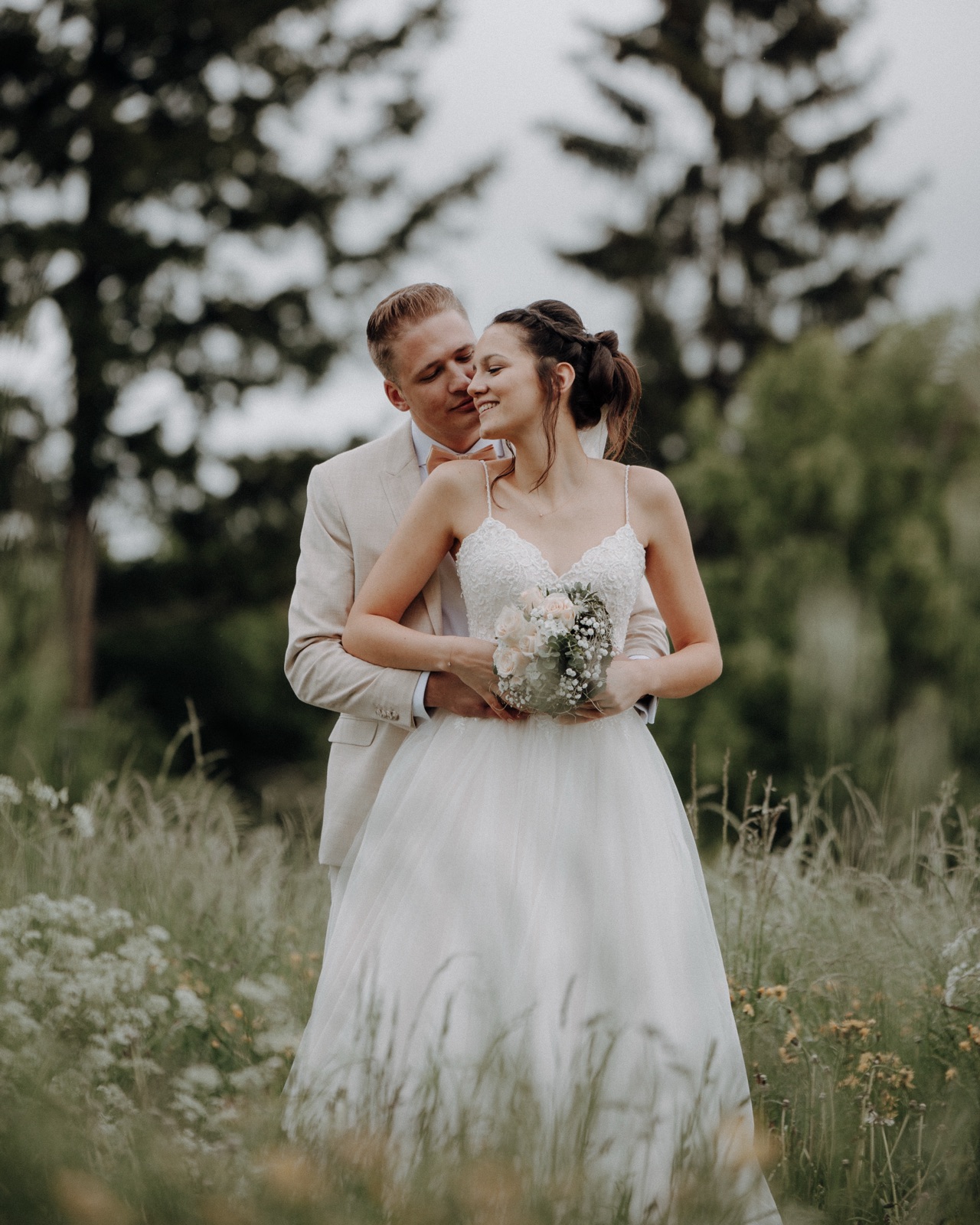 Bräutigam umarmt die Braut zärtlich von hinten in einer Blumenwiese – aufgenommen von einem erfahrenen Hochzeitsfotografen