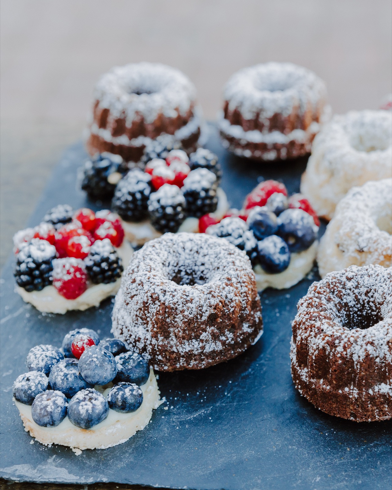 Mini-Gugelhupf-Törtchen mit Beeren und Puderzucker auf Schiefertablett